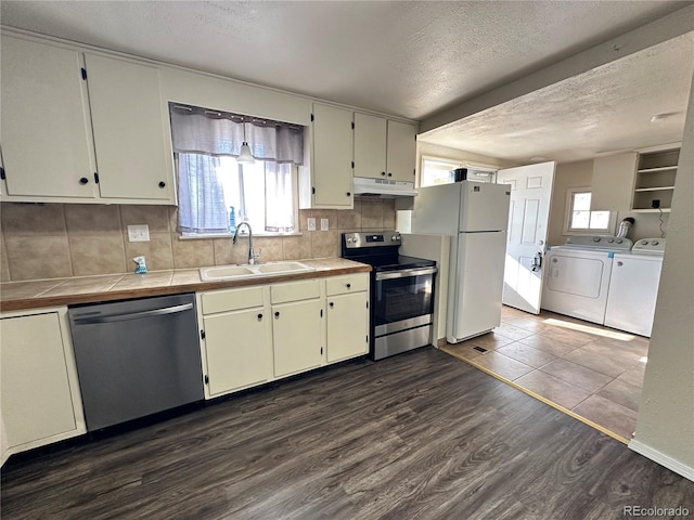 kitchen featuring appliances with stainless steel finishes, washing machine and dryer, dark hardwood / wood-style flooring, sink, and tile countertops