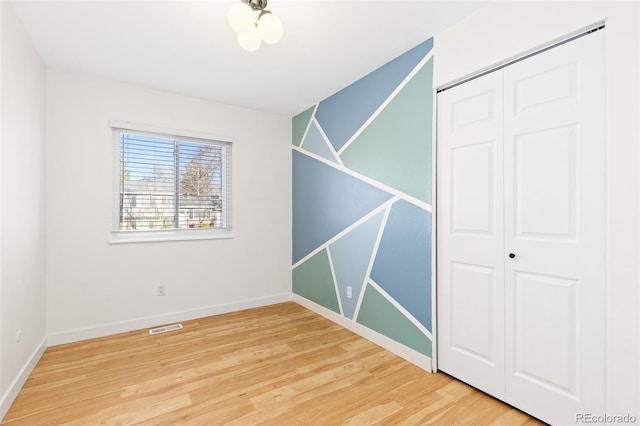 unfurnished bedroom featuring light wood-style flooring, a closet, visible vents, and baseboards