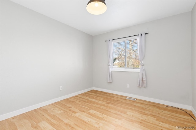 spare room featuring wood finished floors, visible vents, and baseboards