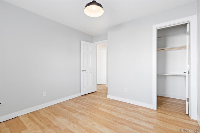 unfurnished bedroom featuring a closet, baseboards, a walk in closet, and wood finished floors