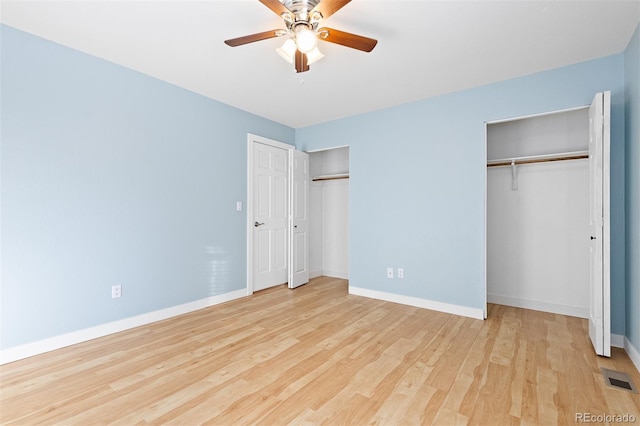 unfurnished bedroom with multiple closets, visible vents, baseboards, and wood finished floors