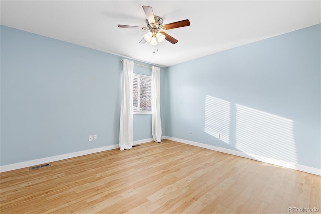 empty room featuring a ceiling fan, visible vents, baseboards, and wood finished floors