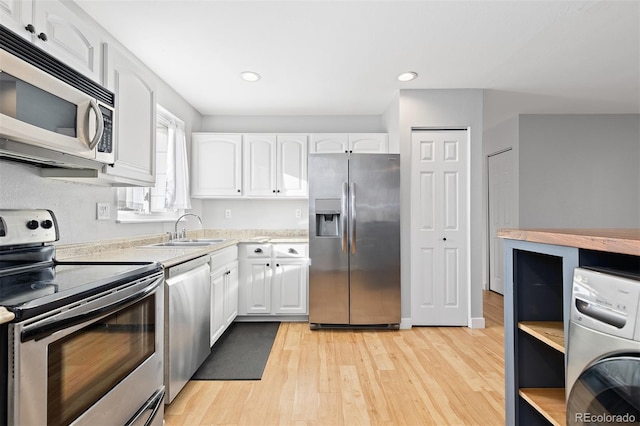 kitchen with a sink, white cabinets, light countertops, appliances with stainless steel finishes, and washer / dryer