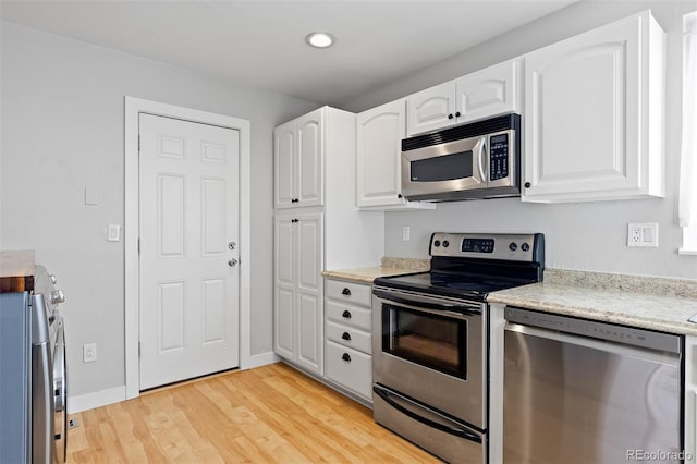 kitchen with light wood finished floors, appliances with stainless steel finishes, baseboards, and white cabinets