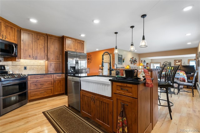 kitchen with stainless steel appliances, a breakfast bar area, light hardwood / wood-style flooring, and a center island with sink