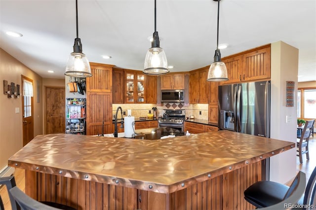 kitchen with appliances with stainless steel finishes, a baseboard radiator, backsplash, hardwood / wood-style floors, and pendant lighting