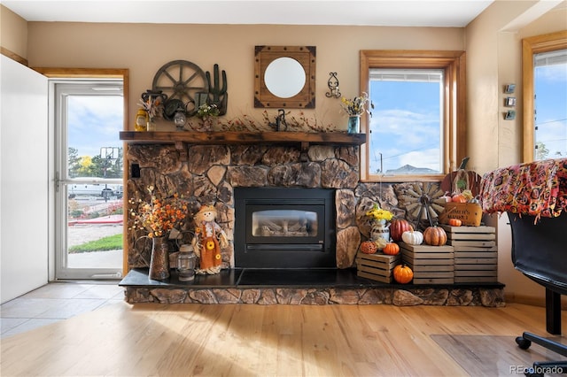 living room with a wealth of natural light, a stone fireplace, and light wood-type flooring