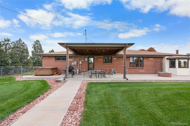 rear view of house featuring a hot tub, a patio area, and a lawn