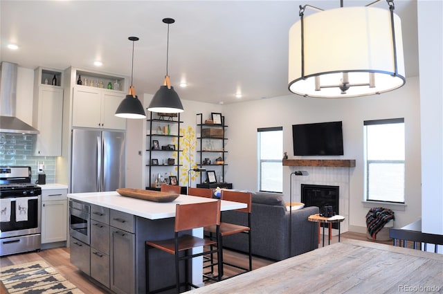 kitchen with appliances with stainless steel finishes, light hardwood / wood-style flooring, backsplash, and wall chimney exhaust hood