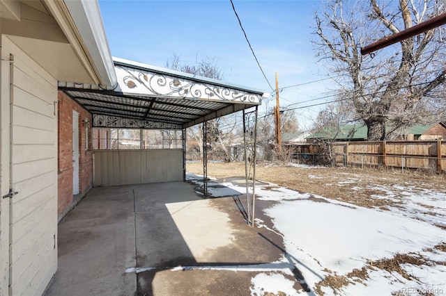 snow covered patio with a carport and fence