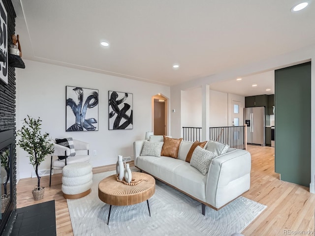 living room with a stone fireplace and light wood-type flooring