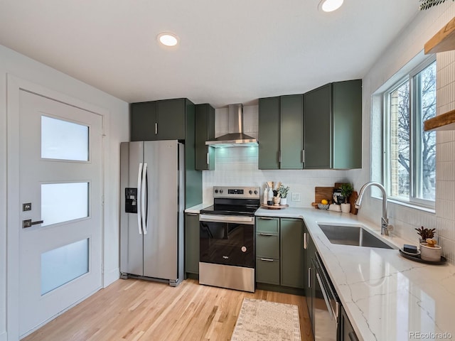 kitchen featuring sink, wall chimney exhaust hood, light stone counters, appliances with stainless steel finishes, and light wood-type flooring