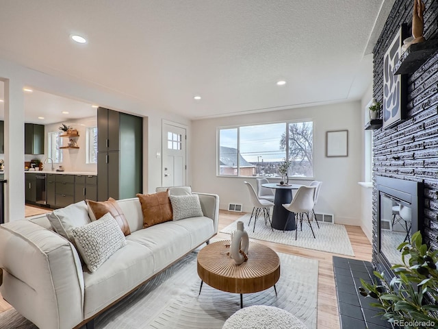 living room with a stone fireplace, a textured ceiling, and light hardwood / wood-style flooring