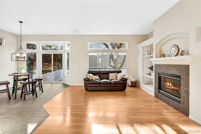 living room featuring a chandelier, a tiled fireplace, light hardwood / wood-style floors, and built in features