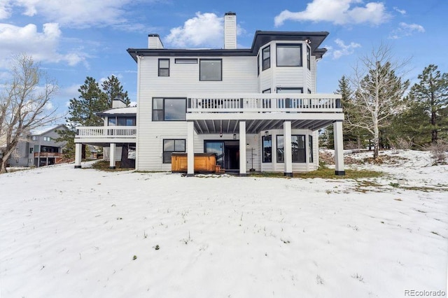 snow covered rear of property featuring a hot tub