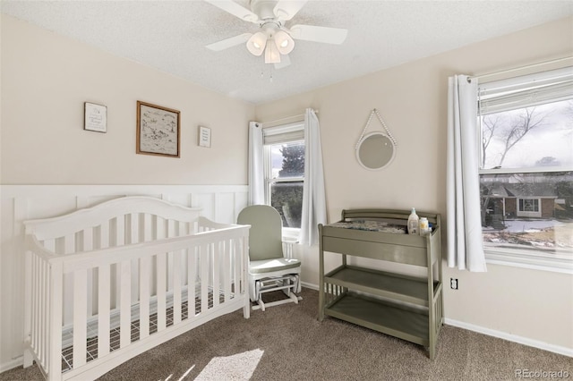 bedroom featuring ceiling fan, dark carpet, a crib, and a textured ceiling