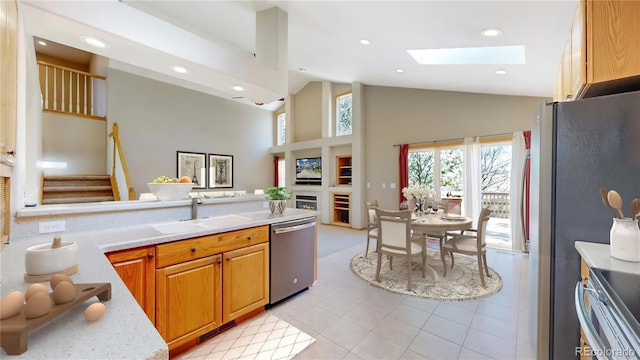 kitchen with a skylight, stainless steel appliances, light countertops, a sink, and high vaulted ceiling