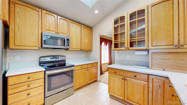 kitchen featuring light tile patterned floors, stainless steel appliances, light countertops, glass insert cabinets, and vaulted ceiling