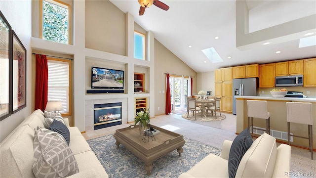 living room featuring high vaulted ceiling, a tile fireplace, recessed lighting, light carpet, and a skylight