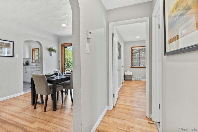 corridor with light hardwood / wood-style flooring, a textured ceiling, and sink