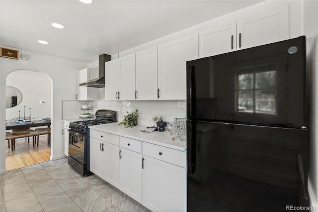 kitchen featuring decorative backsplash, wall chimney range hood, black appliances, white cabinetry, and light hardwood / wood-style floors