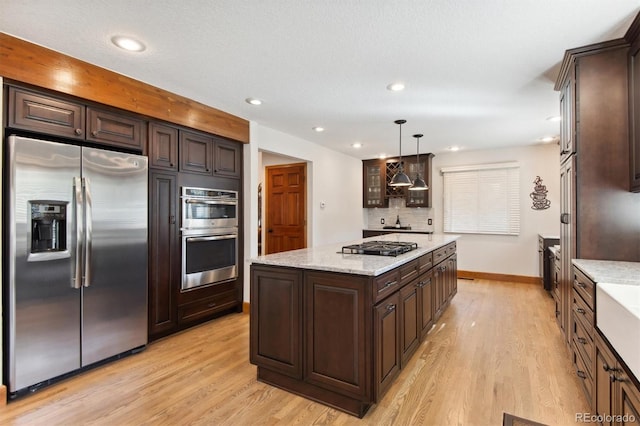 kitchen featuring appliances with stainless steel finishes, pendant lighting, light hardwood / wood-style flooring, and tasteful backsplash