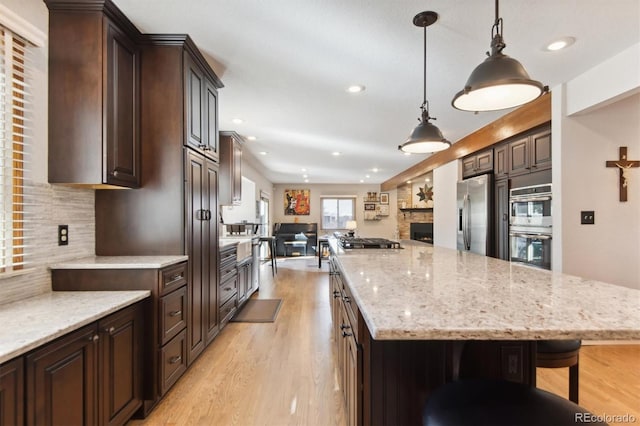 kitchen with decorative light fixtures, a fireplace, backsplash, dark brown cabinets, and appliances with stainless steel finishes