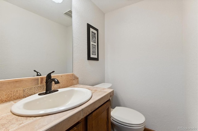 bathroom with vanity, decorative backsplash, and toilet