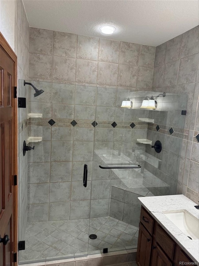 bathroom featuring a textured ceiling, a shower with door, and vanity