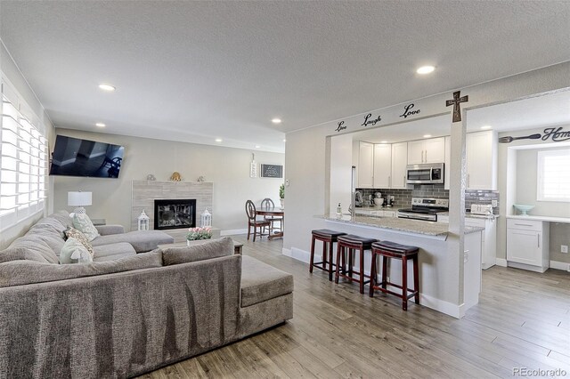 living room with baseboards, light wood-style flooring, recessed lighting, a textured ceiling, and a tiled fireplace