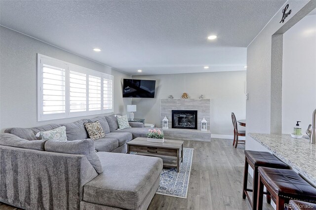 living room with a tiled fireplace, light wood-style flooring, recessed lighting, and a textured ceiling