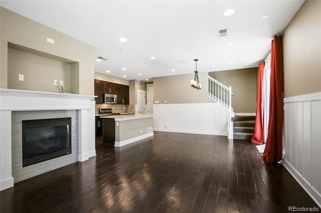 3450 Valentia St, Denver, CO 80238 - unfurnished living room featuring stairway, dark wood-type flooring, a wainscoted wall, a brick fireplace, and a chandelier