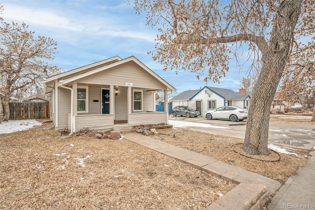 bungalow-style home featuring a porch, concrete driveway, and fence