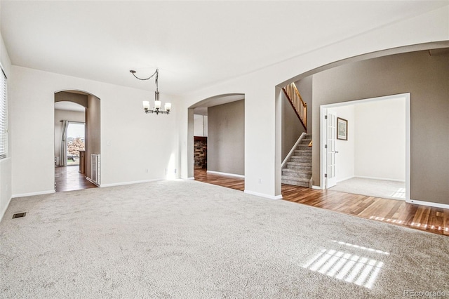 carpeted empty room with visible vents, a notable chandelier, wood finished floors, stairway, and arched walkways