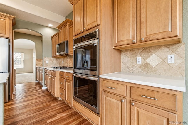 kitchen featuring decorative backsplash, light countertops, arched walkways, and stainless steel appliances