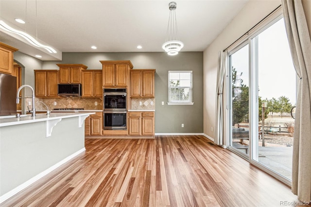 kitchen featuring a sink, tasteful backsplash, stainless steel appliances, light wood-style floors, and light countertops