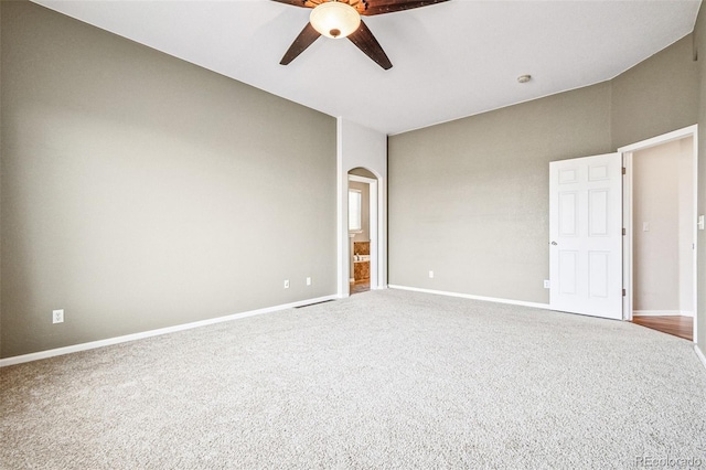 spare room featuring carpet, baseboards, arched walkways, and a ceiling fan