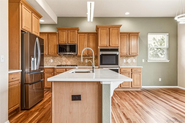 kitchen featuring a center island with sink, a sink, stainless steel appliances, light wood-style floors, and light countertops