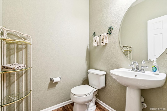 half bath with wood finished floors, baseboards, a sink, toilet, and a textured wall