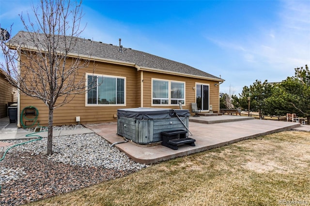 back of house featuring a yard, a patio area, roof with shingles, and a hot tub