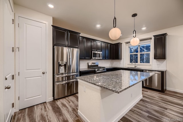 kitchen featuring wood-type flooring, a kitchen island, stainless steel appliances, pendant lighting, and dark stone countertops