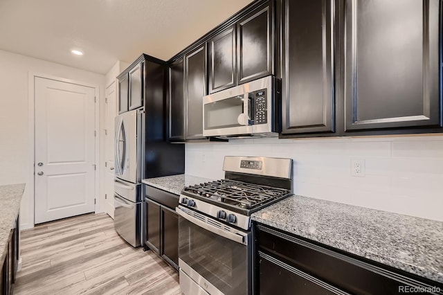 kitchen featuring light stone countertops, appliances with stainless steel finishes, light hardwood / wood-style flooring, and backsplash