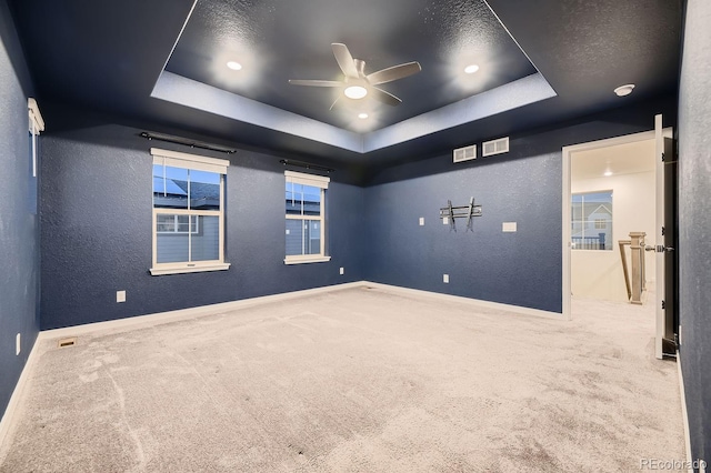 carpeted empty room with ceiling fan and a raised ceiling