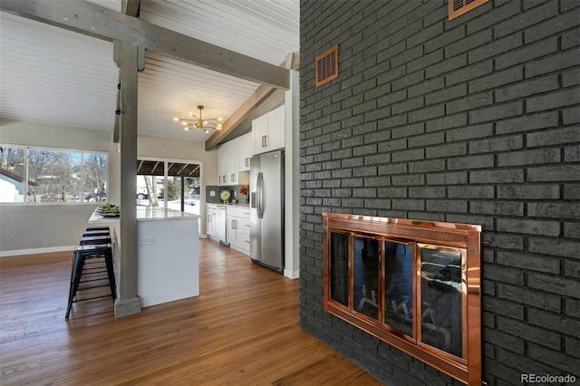 kitchen with white cabinetry, vaulted ceiling with beams, a fireplace, stainless steel fridge with ice dispenser, and a notable chandelier