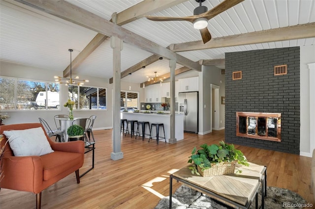 living room with vaulted ceiling with beams, light wood-type flooring, a fireplace, and ceiling fan with notable chandelier