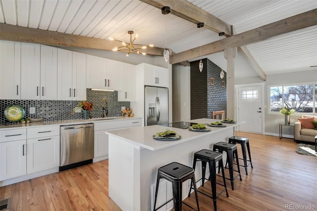 kitchen featuring stainless steel appliances, white cabinetry, hanging light fixtures, and a center island