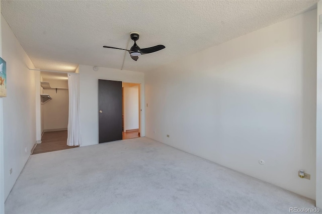 unfurnished bedroom with a spacious closet, ceiling fan, a textured ceiling, light carpet, and a closet