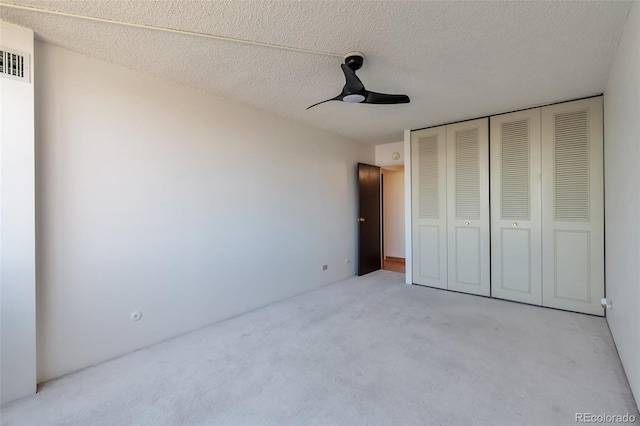 unfurnished bedroom featuring ceiling fan, a textured ceiling, light carpet, and a closet