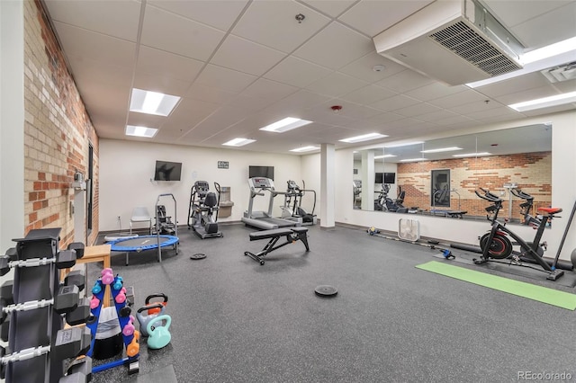 workout area with a paneled ceiling and brick wall