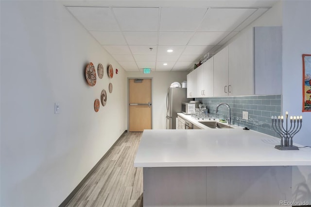 kitchen featuring a drop ceiling, backsplash, white cabinets, sink, and kitchen peninsula